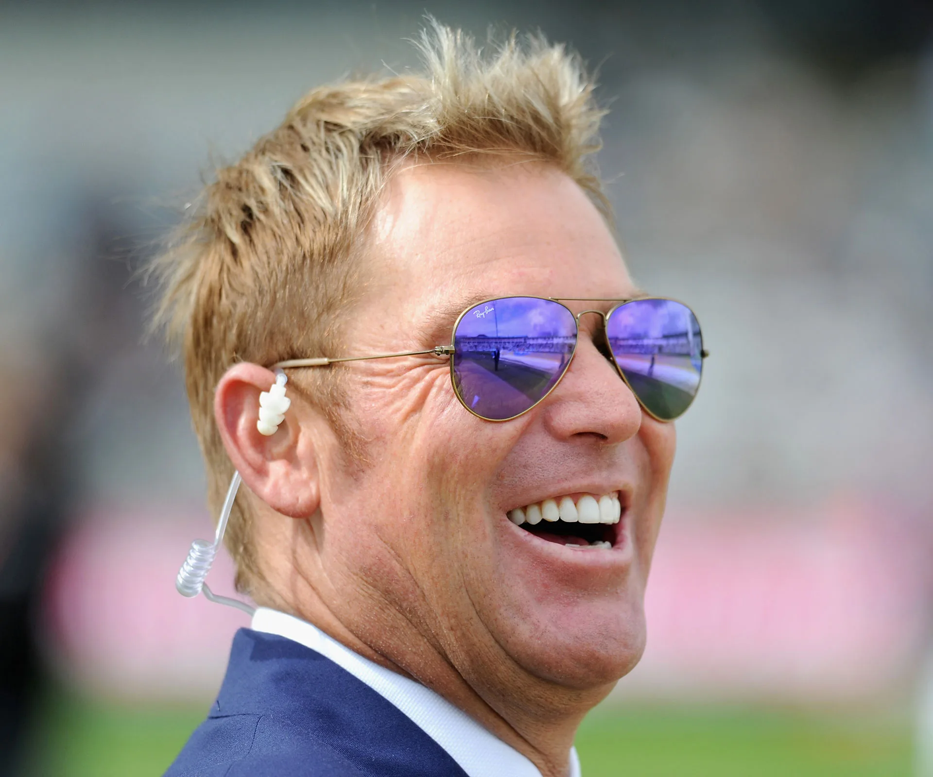 A man wearing sunglasses and a suit, smiling broadly, with an earpiece.