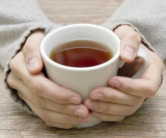 Hands holding a warm cup of tea on a wooden table.