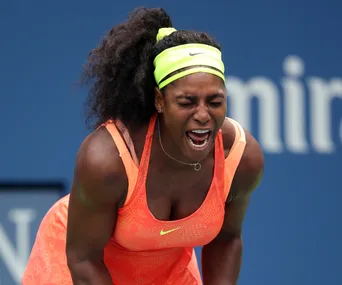 A tennis player wearing an orange top, expressing a strong emotion during a match.