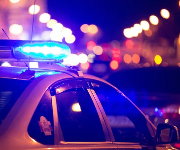 Police car with flashing lights at night, blurred city lights in the background.