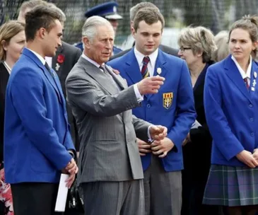Man in a suit talks with students in blue uniforms during an outdoor event.