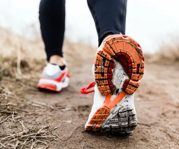 Close-up of a person's sneakered foot stepping on a dirt path during a walk.