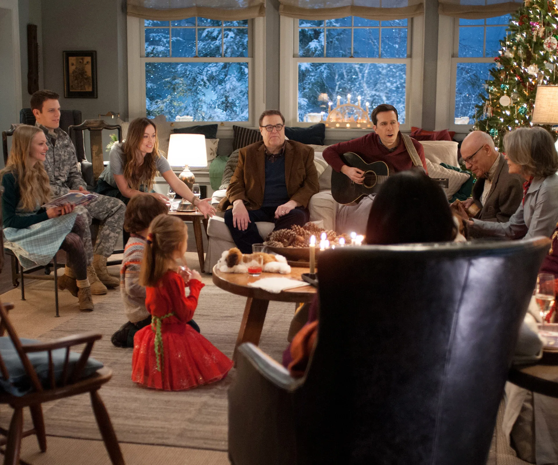 Family gathered in a cozy living room at Christmas, with a decorated tree, a guitar, and snowy scenery outside the window.