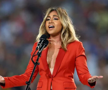 Singer in a red blazer performs passionately on stage with a microphone.