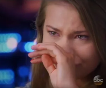 Young woman wiping tears, blue and pink lights in background.