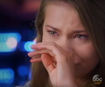 Young woman wiping tears, blue and pink lights in background.