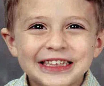 Smiling young boy with light brown hair and bright eyes in a close-up portrait.