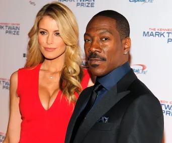 Two people posing at the Kennedy Center Mark Twain Prize event; one in a red dress, the other in a black suit.