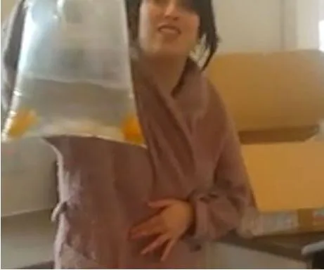 Woman holding a bag of live fish with a surprised expression, standing next to an open cardboard box.