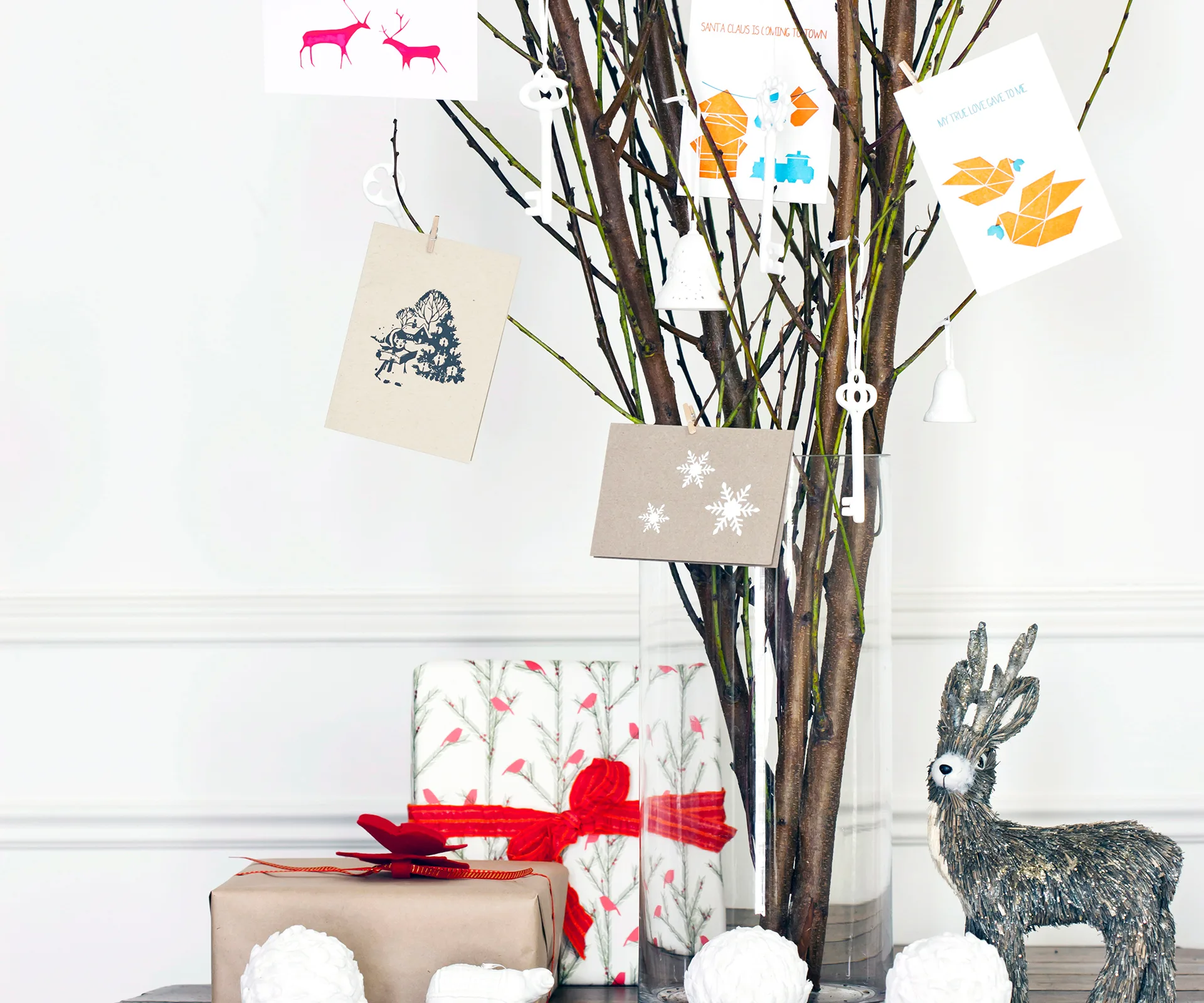 A festive display with a twig tree holding cards, wrapped gifts, and a decorative deer figurine.