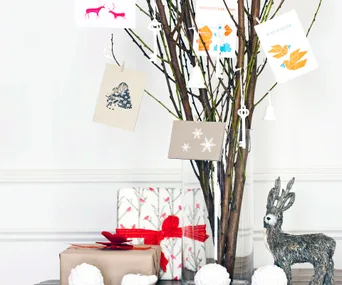 A festive display with a twig tree holding cards, wrapped gifts, and a decorative deer figurine.