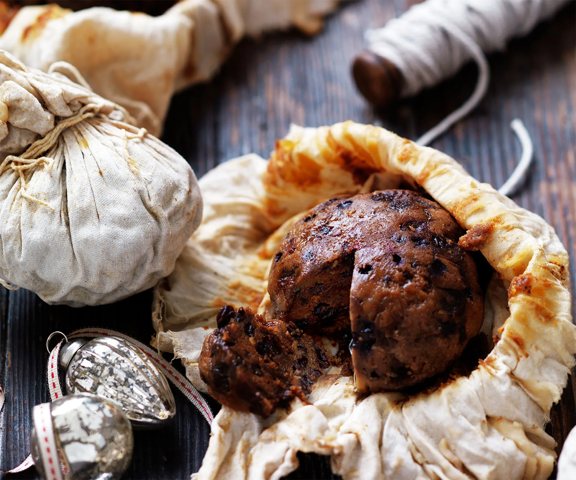 Plum pudding wrapped in cloth, with festive decorations and twine on a wooden table.