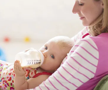 Mother holding baby drinking from a bottle, highlighting care and feeding in a cozy setting.