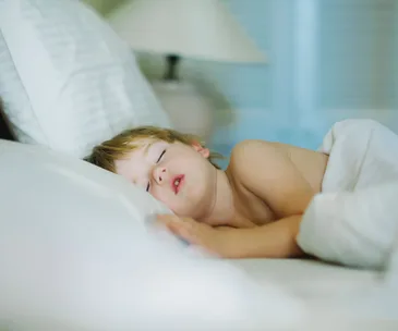 A young child peacefully sleeping in a bed, wrapped in a white blanket.