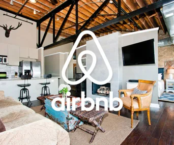 Airbnb rental interior with modern decor, featuring a kitchen, sitting area, and large logo in foreground.