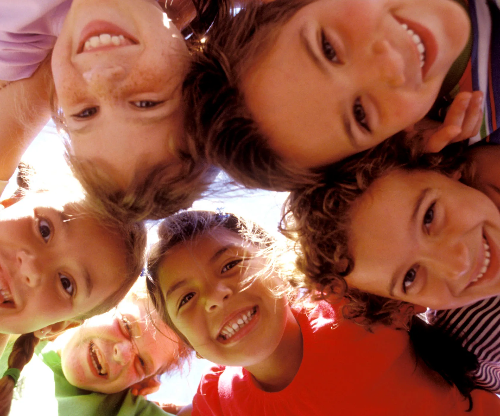 Group of smiling children looking down at the camera outdoors, with a clear sky background.