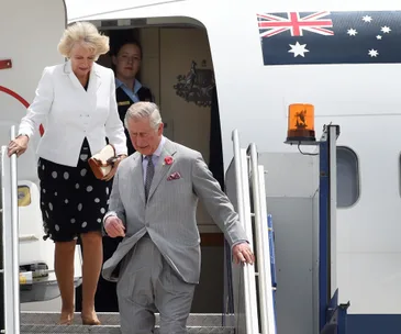 Prince Charles and Camilla exit a plane in Australia, with an Australian flag above the door.