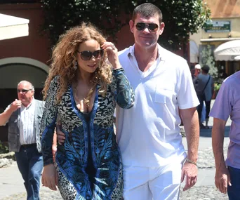 Couple walking arm-in-arm; woman in blue patterned dress, man in white shirt, both wearing sunglasses.