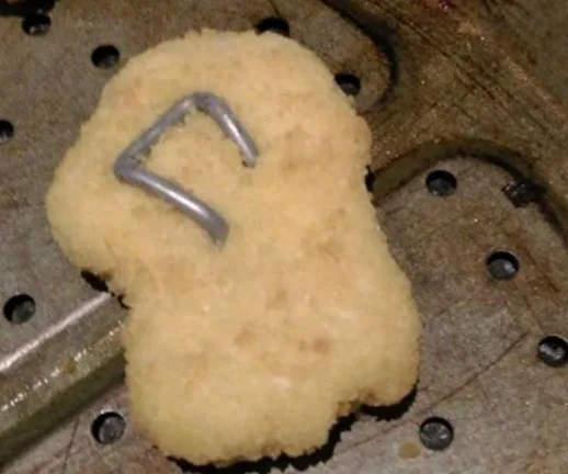 Chicken nugget with a metal piece on a metallic baking sheet.