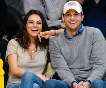 A smiling couple sitting together at a sports event, woman resting hand on man's shoulder.