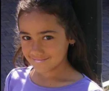 Young girl with long hair smiling and wearing a purple top.