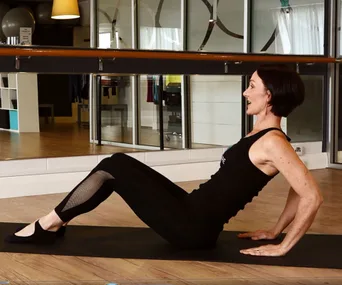 A woman in workout attire performs tricep dips on a yoga mat in a fitness studio with mirrored walls.