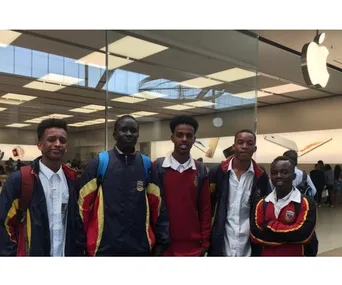 Five students in school uniforms outside an Apple Store, smiling at the camera.