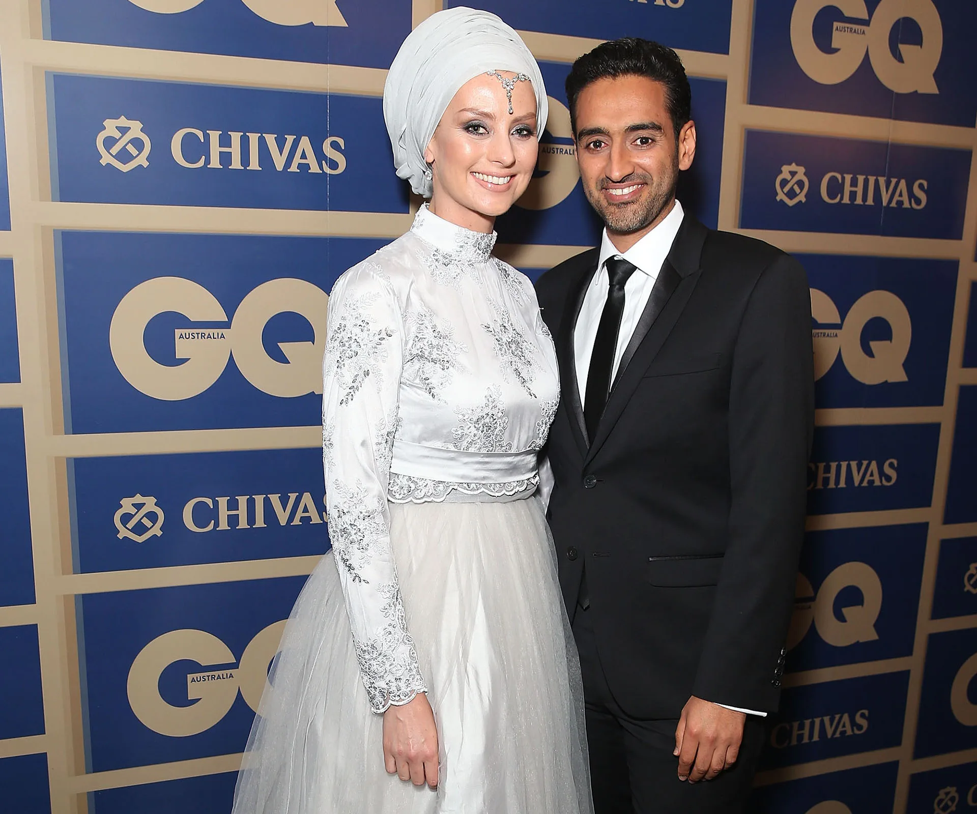 A couple posing at a GQ event, smiling, with a Chivas banner in the background.
