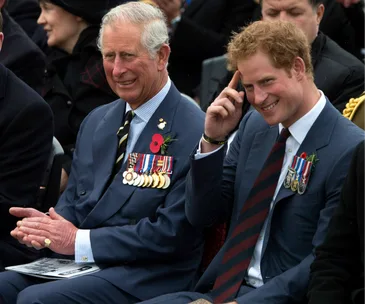 Two men in suits with military medals, sitting and smiling at an outdoor event.