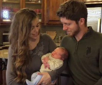 Family holding their newborn baby in a warm kitchen setting, smiling at the infant.