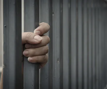 Hand gripping metal prison bars, representing confinement and imprisonment.