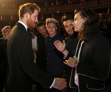 Prince Harry shakes hands with members of a band at an event in a theater setting.