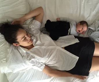 Mother and baby lying together on a bed, both gazing peacefully.
