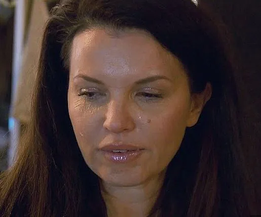 A woman with long dark hair appears emotional, looking downward with a tear on her cheek.