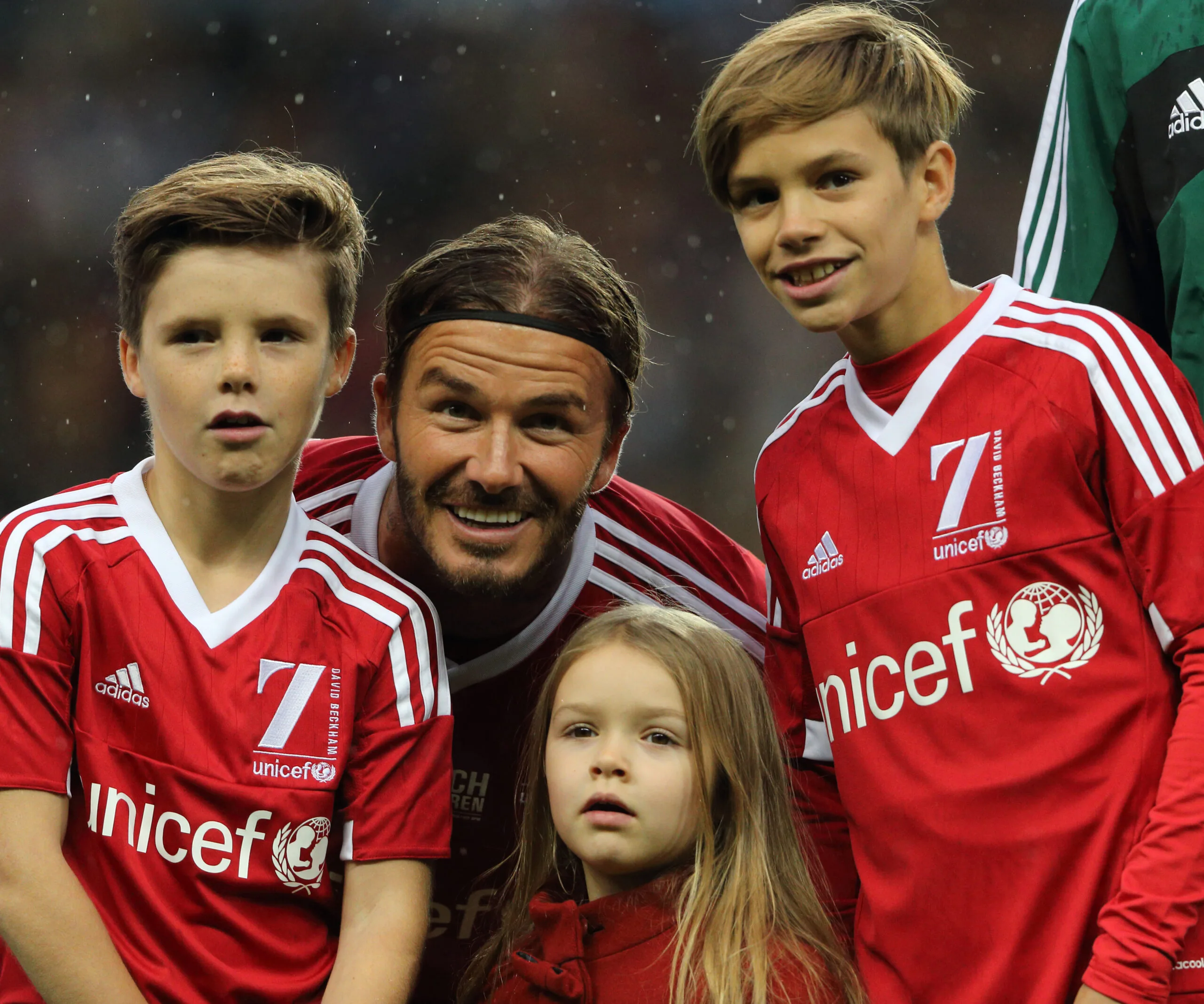 "David Beckham with three children in red UNICEF soccer jerseys on a field."