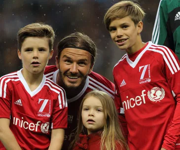 "David Beckham with three children in red UNICEF soccer jerseys on a field."