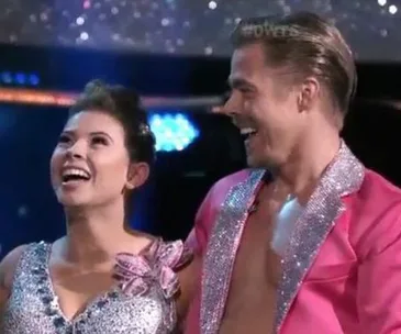 Two dancers in sparkly outfits smile and celebrate on a brightly lit stage.