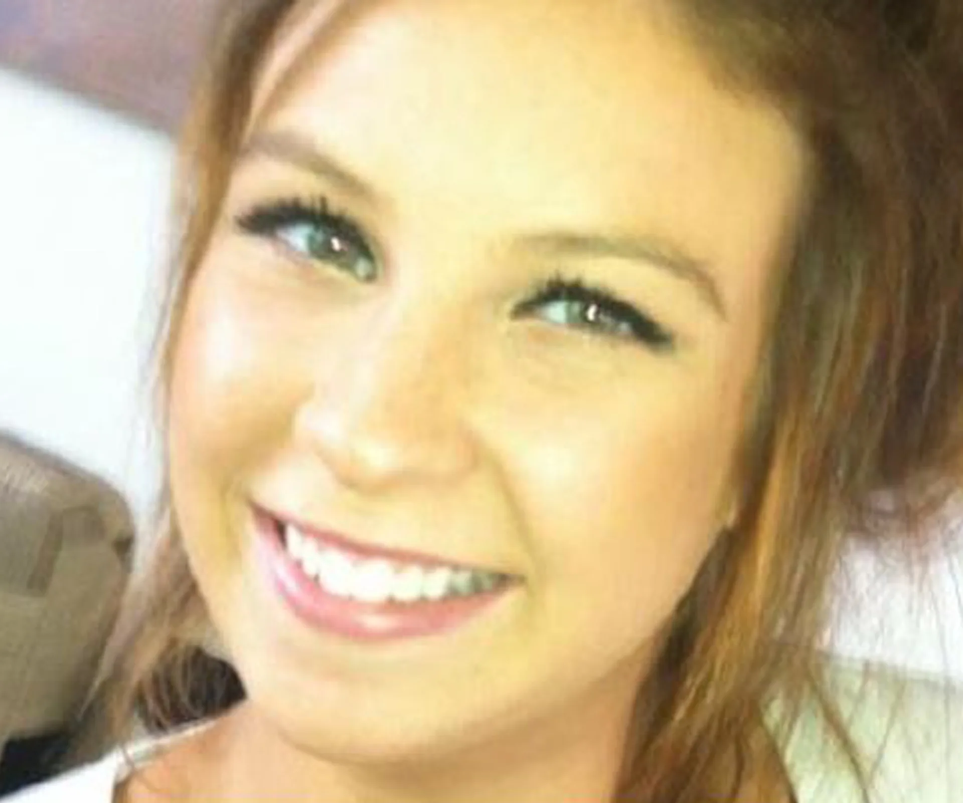 A young woman with long hair smiling in a close-up photo indoors.