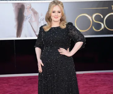 A woman in a black sequined dress stands on a red carpet at an event, with a backdrop featuring an illustration.