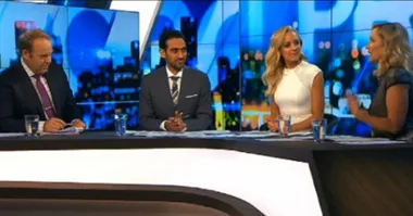 Panel sitting at a news desk with a cityscape background.