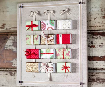 DIY advent calendar with wrapped boxes and bows on a fabric board.