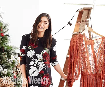 Woman in floral dress smiling beside Christmas tree and lace dress on a ladder.