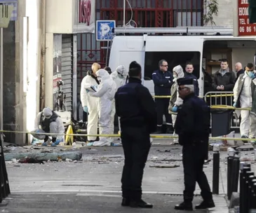 Forensic teams and police officers examine debris and secure a street after a raid.