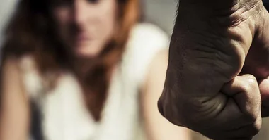 A clenched fist in focus with a blurred person in the background, conveying tension or conflict.