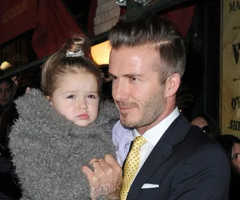 Father in suit holding his young daughter wrapped in a fluffy gray coat, surrounded by a bustling city background.