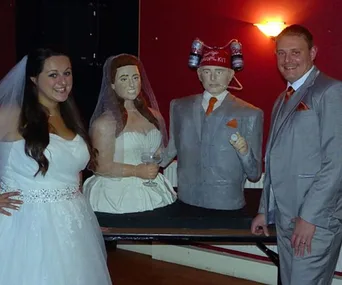 Bride and groom pose with life-sized wedding cake replicas of themselves.
