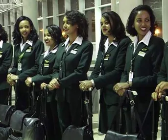 All-women crew of Ethiopian Airlines in uniform, standing in a row at an airport terminal, smiling with luggage.