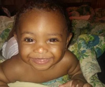 A smiling baby lying on a floral-patterned blanket.