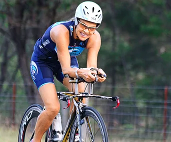 Cyclist in a Warringah jersey riding a bike intensely, wearing a helmet and sunglasses.