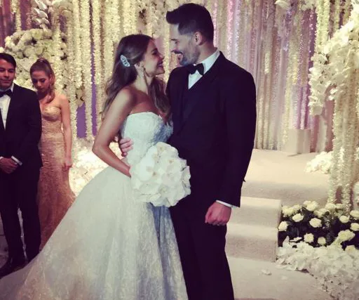 Bride and groom smiling at each other in a lavish wedding setting with white flowers and light-colored decor.